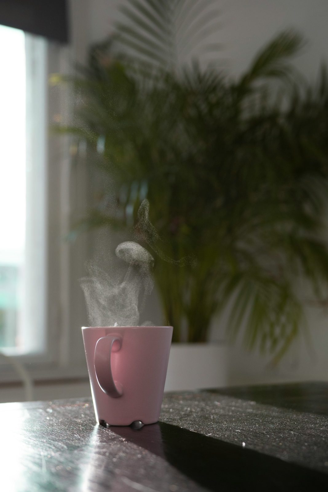 A steaming pink mug on a dark table